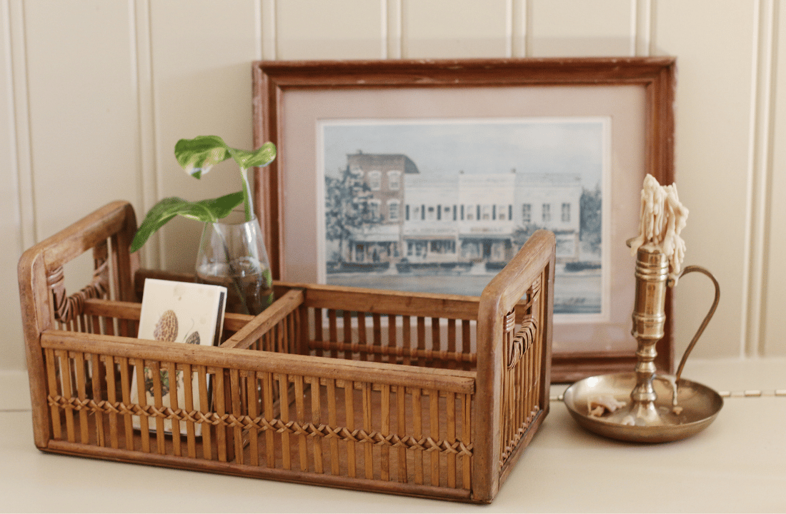 basket with matchbox and plant with framed art behind it next to candle stick