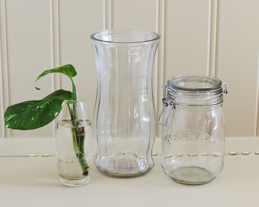 3 thrifted glass jars with a plant in one on a bench