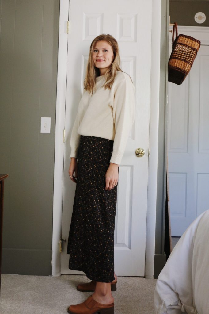 woman in thrifted sweater and skirt standing in front of closet