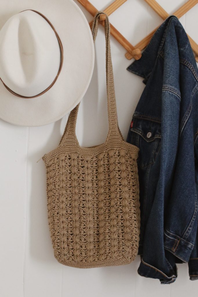 tan knit purse hanging next to white hat and denim jacket