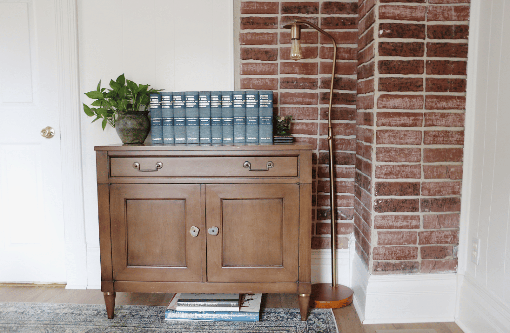 wood console with blue books and plant on top next to floor lamp in styled home