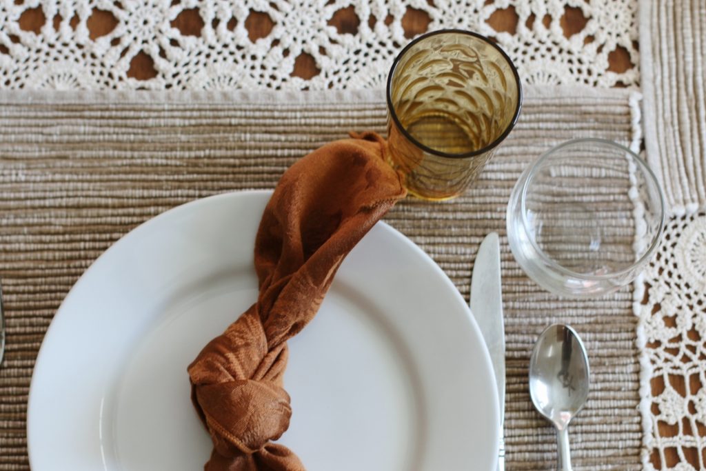 place setting with plate, rust napkin, silverware, and glass