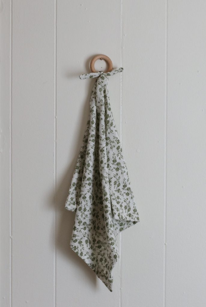 lovey teether baby blanket with wood ring hanging on white wall