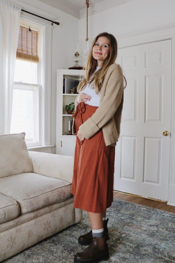 pregnant women wearing skirt, boots, and sweater in living room