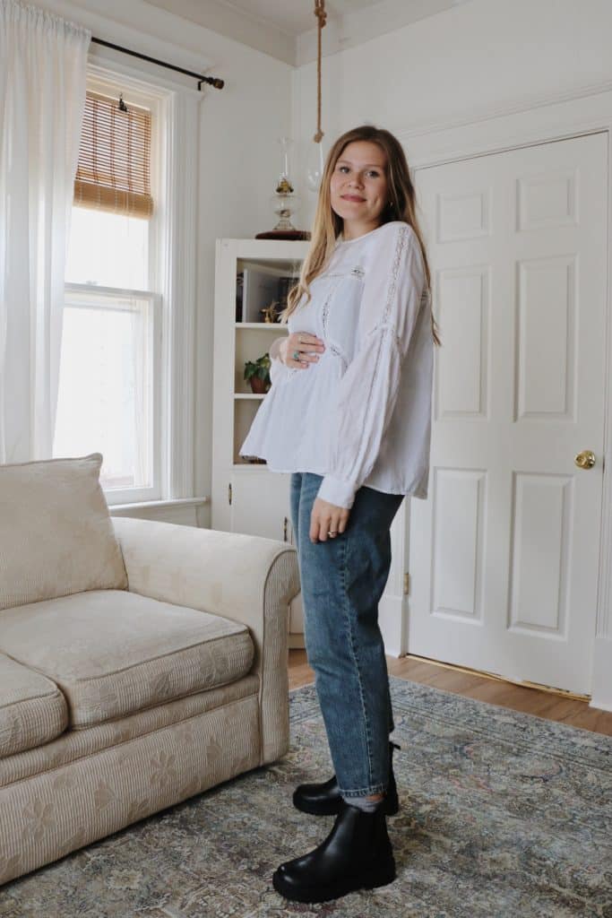 pregnant woman wearing white blouse with denim jeans and black boots in living room