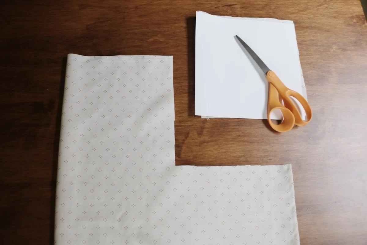 cut square and scissors next to cut fabric on wood table